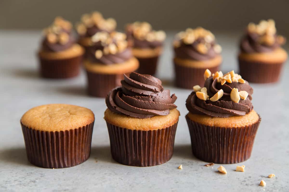 three peanut cupcakes: one unfrosted, second with chocolate frosted, third with chocolate frosting and chopped peanuts.