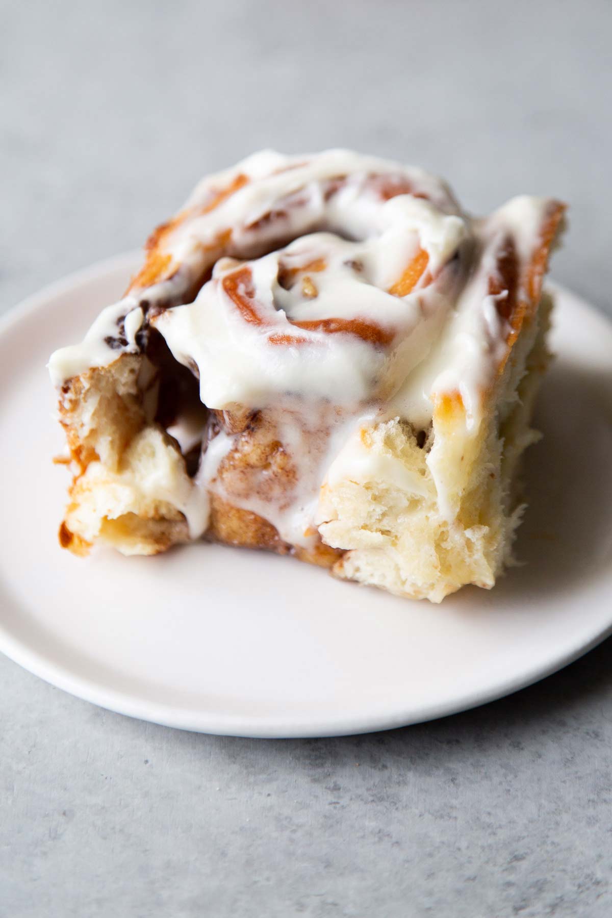 soft and fluffy banana cinnamon roll with cream cheese glaze on white serving plate. 