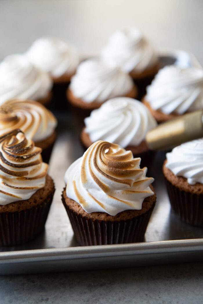 sheet tray filled with meringue topped cupcakes ready to be torched.