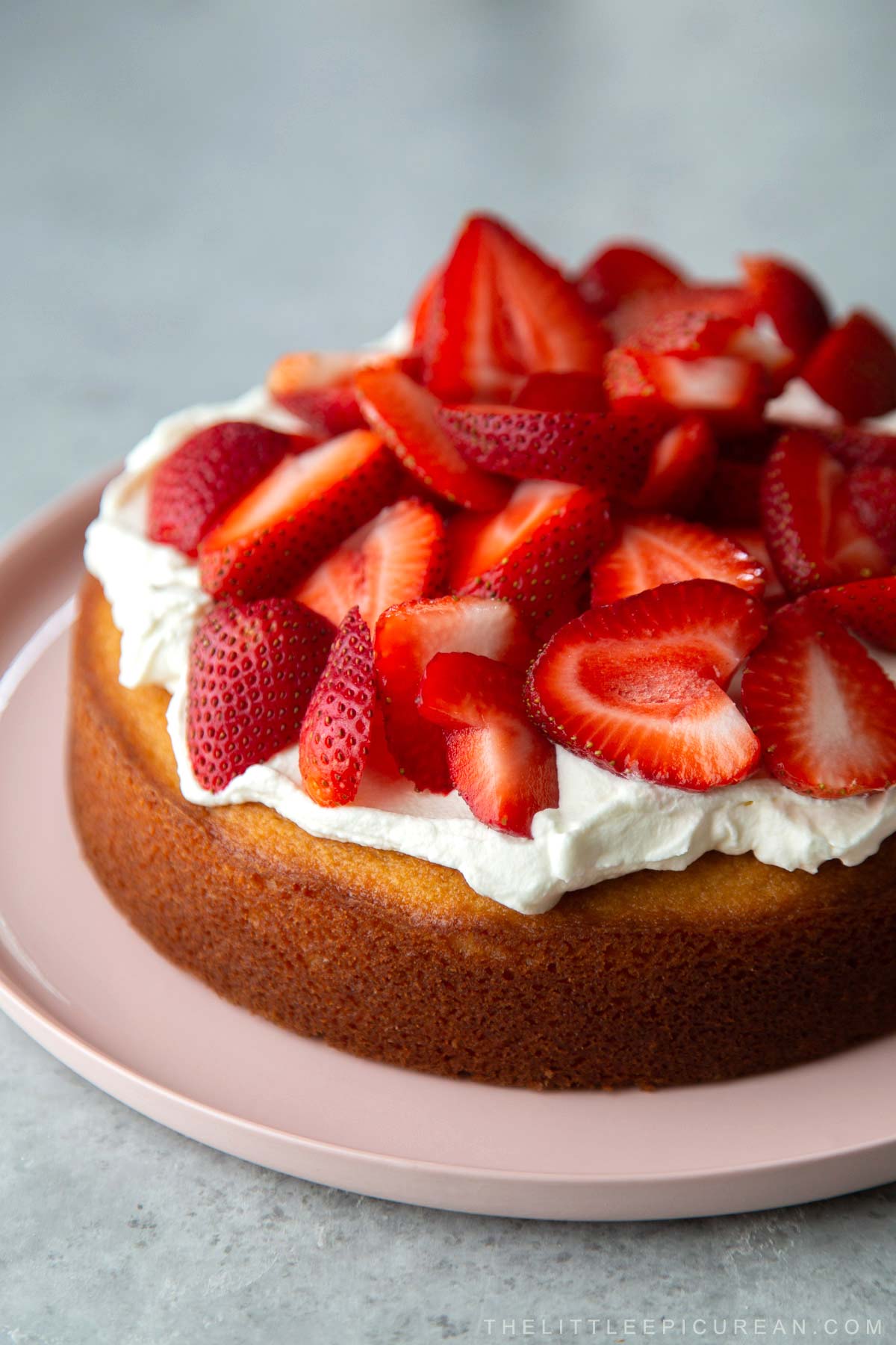 single layer almond cake topped with whipped cream and fresh strawberries on pink serving plate.