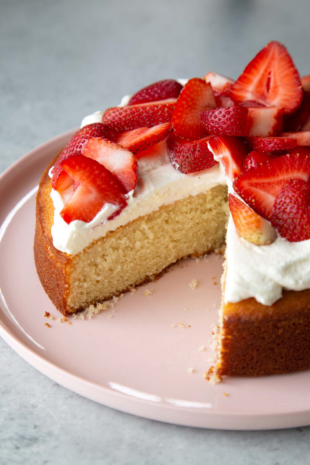 wedge taken out of single layer almond cake topped with whipped cream and fresh strawberries.