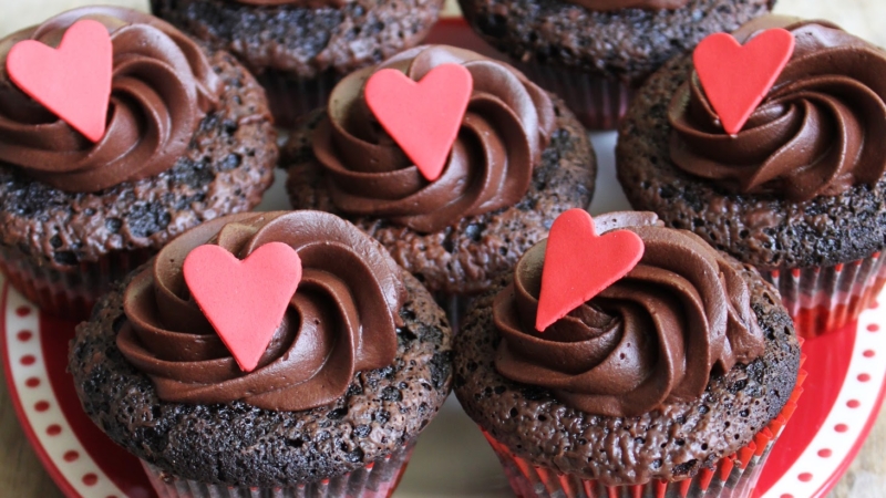 dark chocolate cupcakes with chocolate frosting and heart decor on red plate.