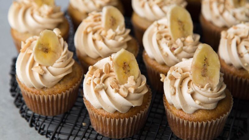 banana cupcakes with peanut butter frosting on black wire rack.