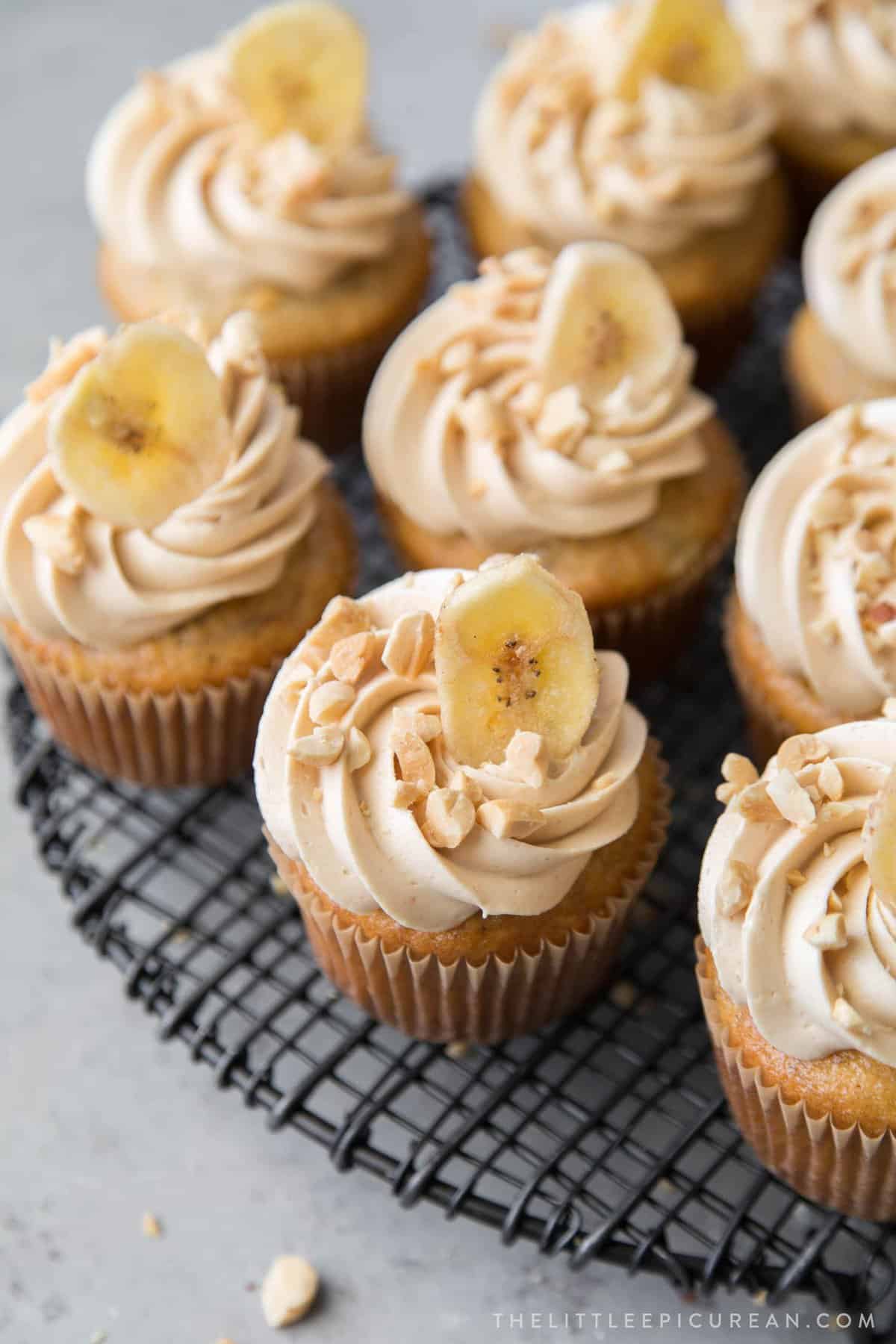 banana cupcakes with piped peanut butter buttercream topped with banana chip and chopped peanuts.