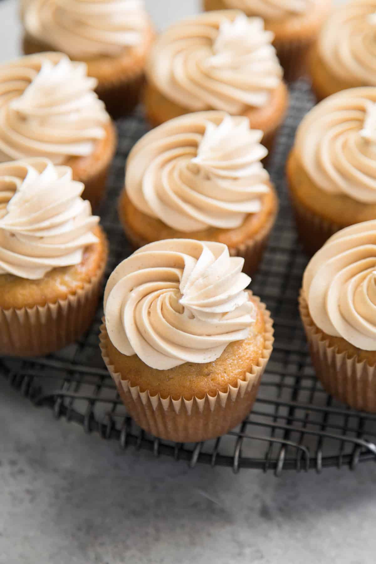 banana cupcakes with peanut butter frosting on black wire rack.