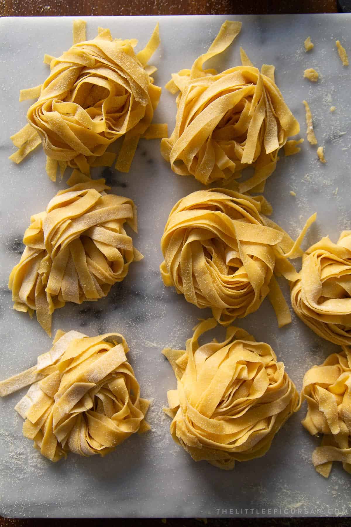 6 bunches of fresh fettuccine pasta on marble surface.