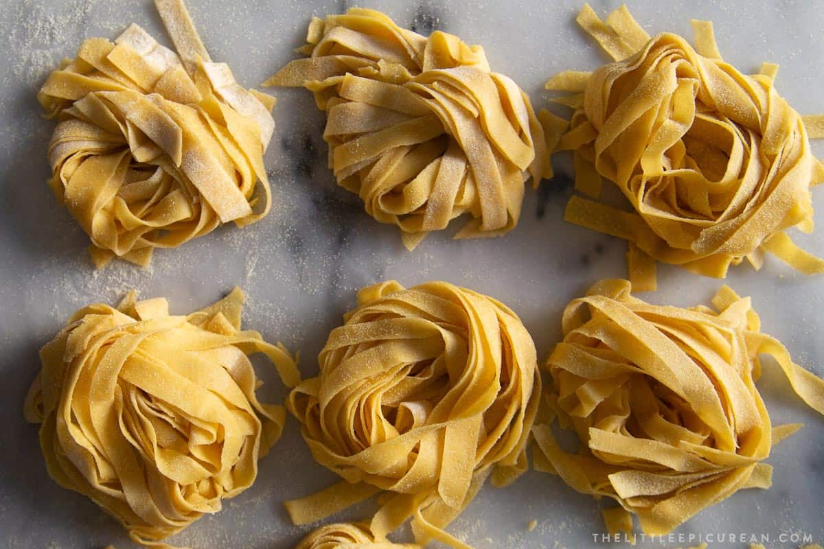 six portions of fresh pasta noodles arranged on marble surface.