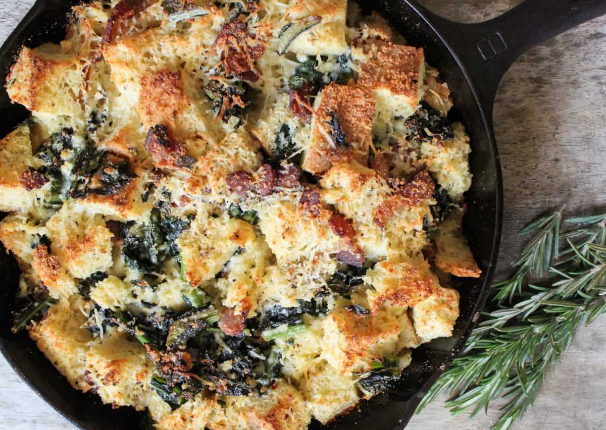 Savory Parmesan Bread Pudding with Bacon, Kale, and Rosemary in cast iron pan. 