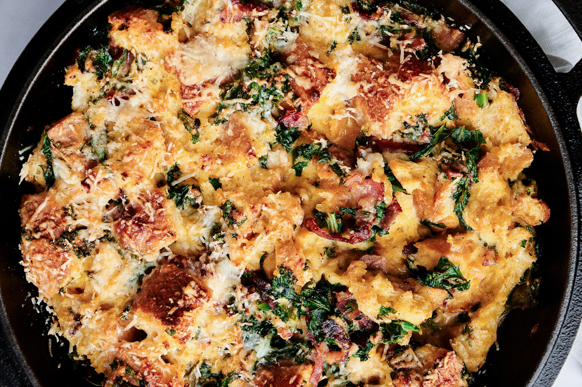 savory bread pudding featuring bacon and kale in black cast iron pan.