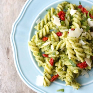 Fusilli with arugula pesto, sun-dried tomatoes, and shaved pecorino on blue plate.