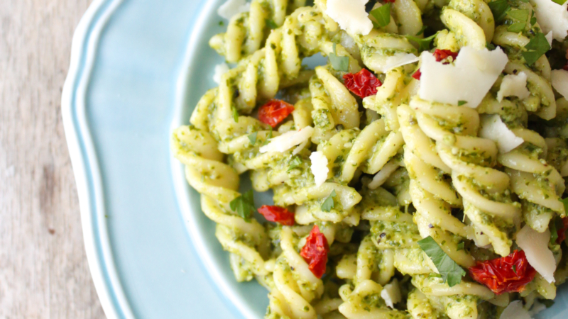 Fusilli with arugula pesto, sun-dried tomatoes, and shaved pecorino on blue plate.