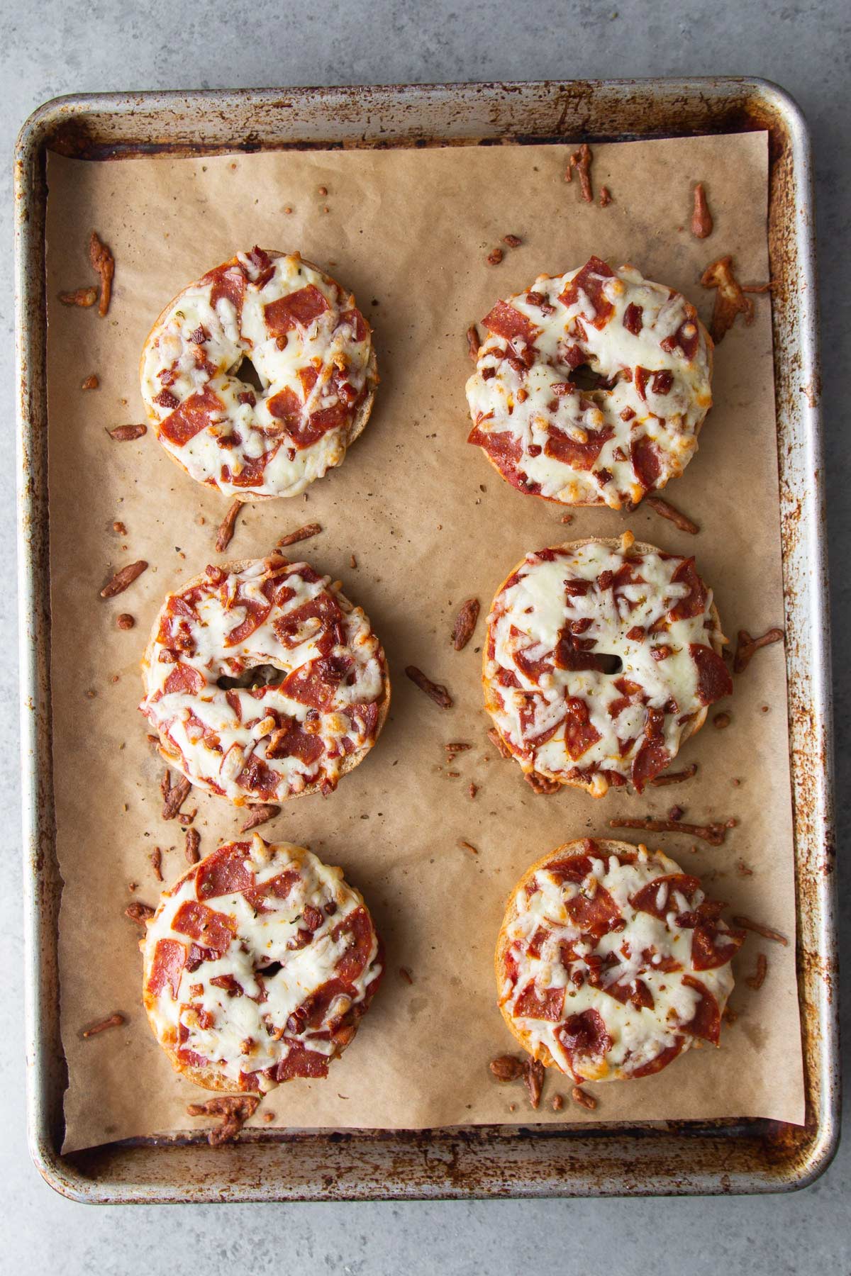 homemade pizza bagels topped with sauce, cheese, pepperoni, and pancetta on baking sheet.