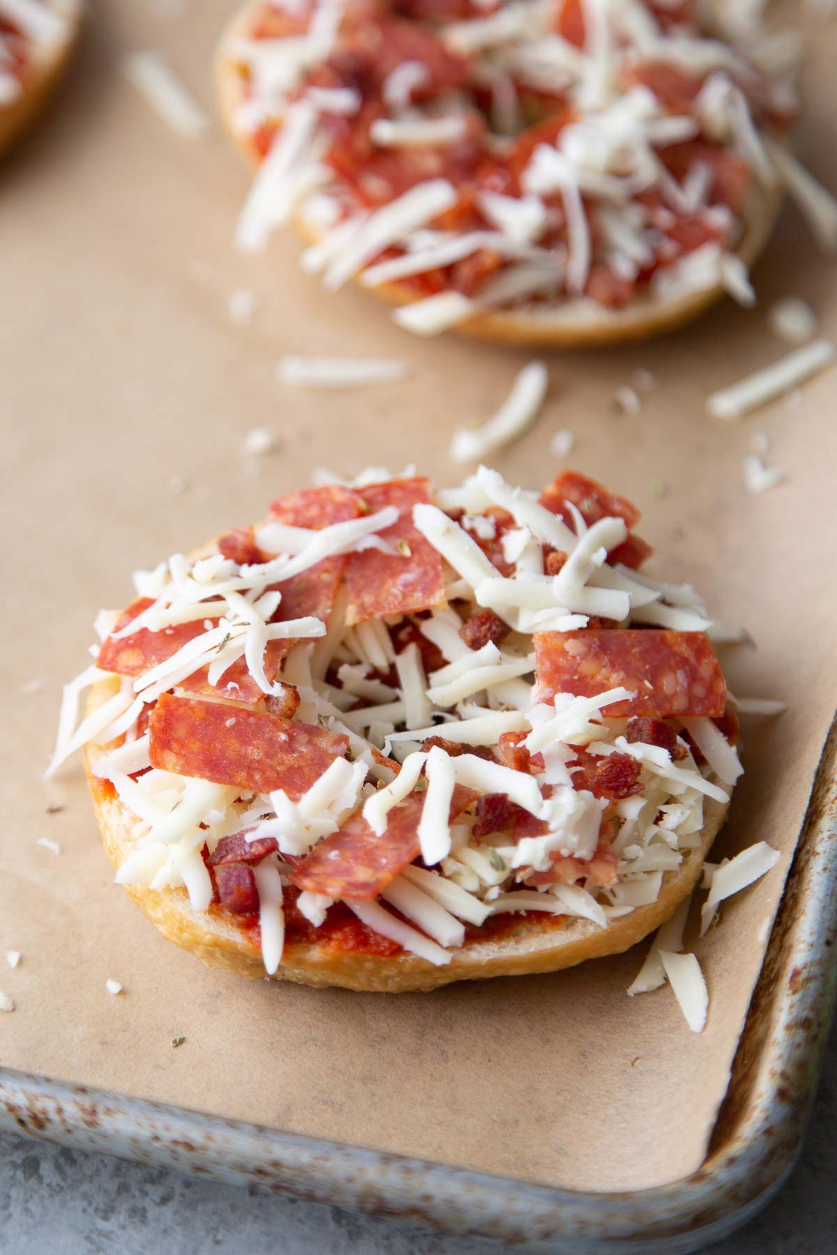 tomato sauce, shredded mozzarella, and pepperoni atop bagel on baking sheet.