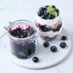 blueberry jam in a glass jar alongside parfait made with blueberry jam and yogurt.