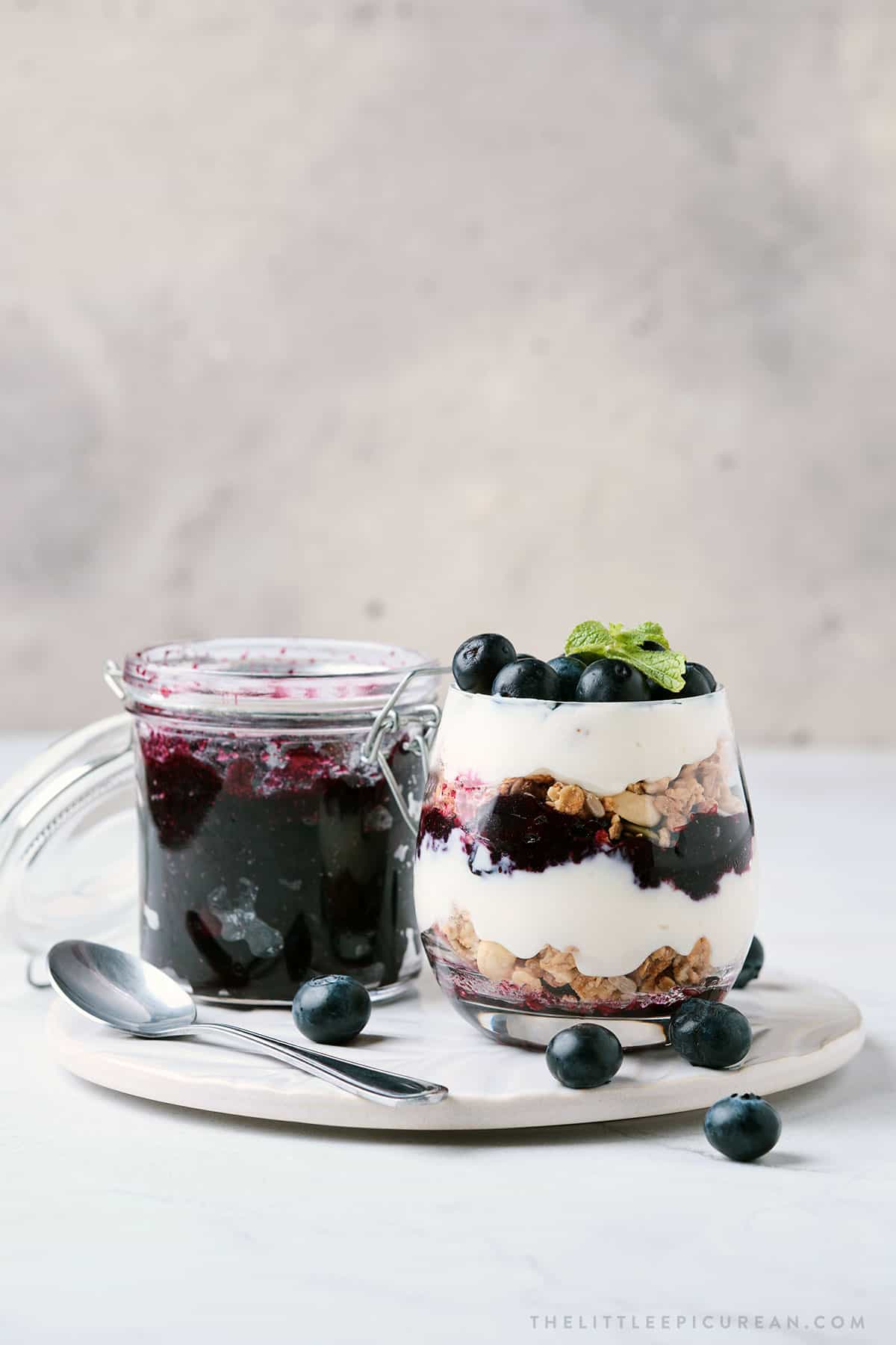 refrigerator blueberry jam along side layered parfait made with yogurt, granola, and blueberry jam.