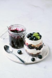 refrigerator blueberry jam along side layered parfait made with yogurt, granola, and blueberry jam.