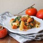 roasted persimmon pasta with arugula, cheddar, and parmesan on white plate.