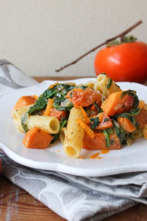 roasted persimmon pasta with arugula, cheddar, and parmesan on white plate.