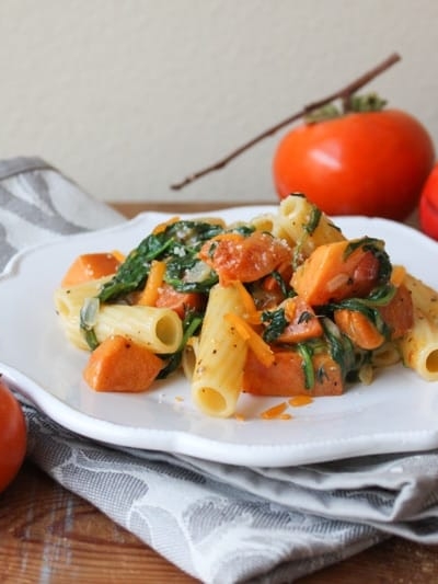 roasted persimmon pasta with arugula, cheddar, and parmesan on white plate.