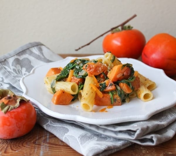 roasted persimmon pasta with arugula, cheddar, and parmesan on white plate.
