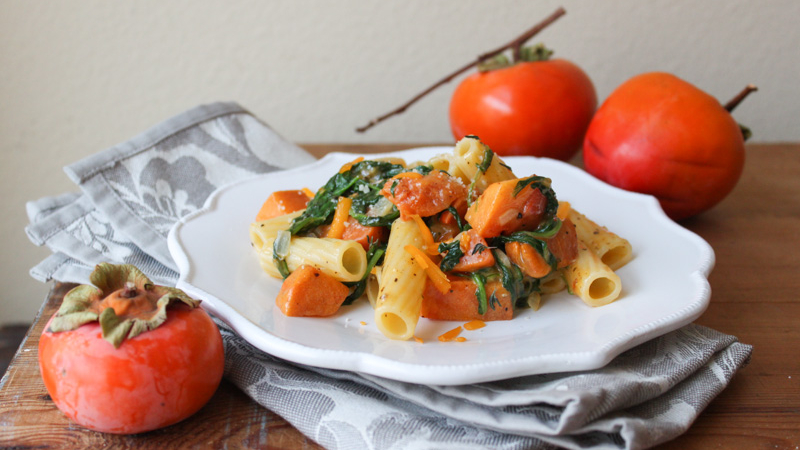 roasted persimmon pasta with arugula, cheddar, and parmesan on white plate.