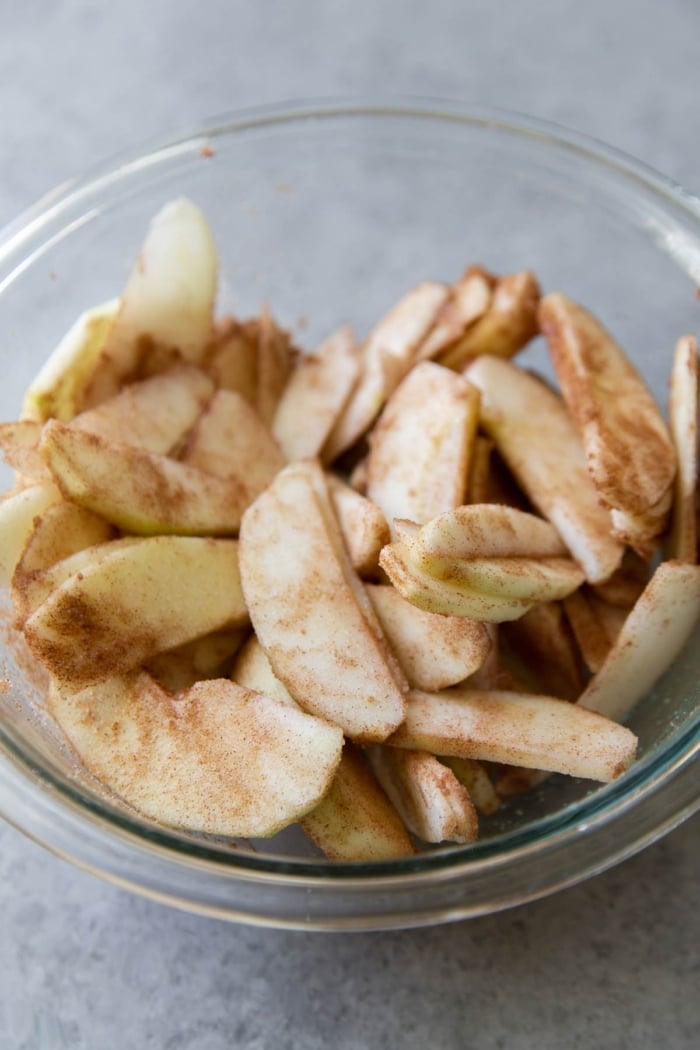 thinly sliced apples tossed with cinnamon, sugar, and lemon juice in a glass bowl.