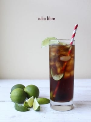 Cuba Libre in a tall glass garnished with limes.