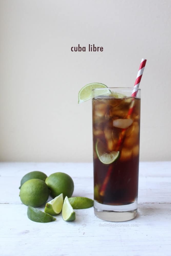 Cuba Libre in a tall glass garnished with limes.