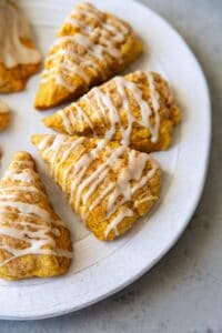 pumpkin scones with maple glaze drizzle on serving plate.