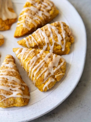 pumpkin scones with maple glaze drizzle on serving plate.