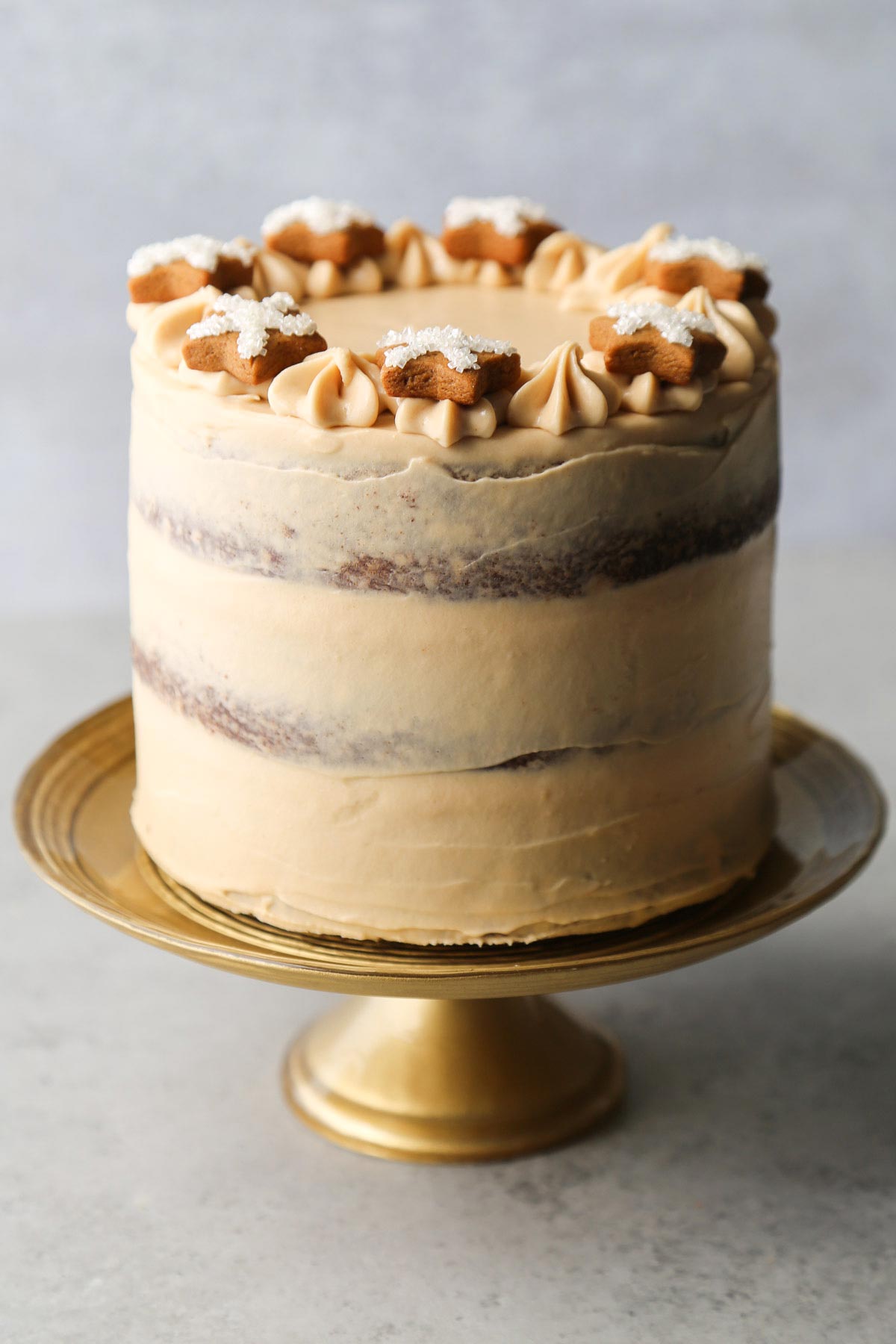 gingerbread layer cake decorated with gingerbread star cookies on gold cake stand.