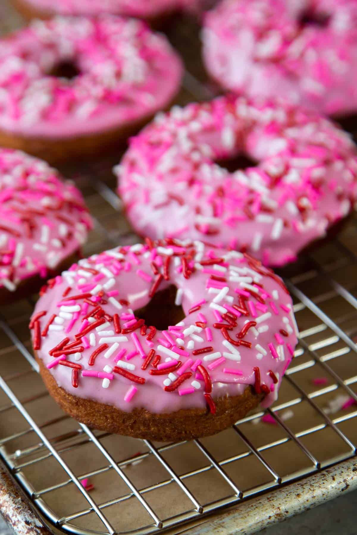 pink glazed cake donuts with sprinkles on wire rack.