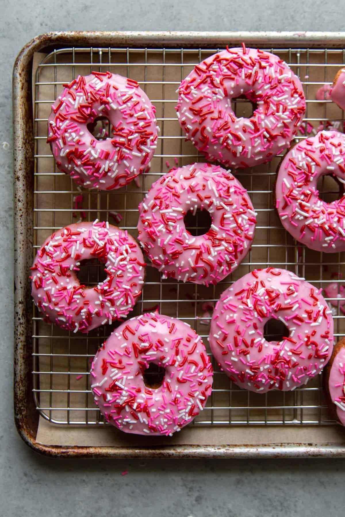 pink glazed donuts with valentine's sprinkles on wire rack. 