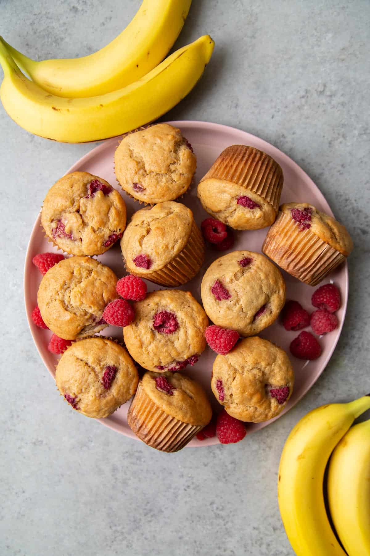 overhead of buttermilk banana muffins with raspberries on pink serving plate.