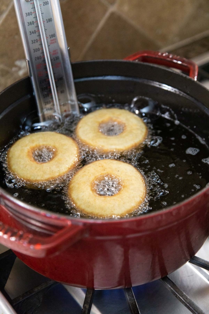 three donuts frying pot of oil.