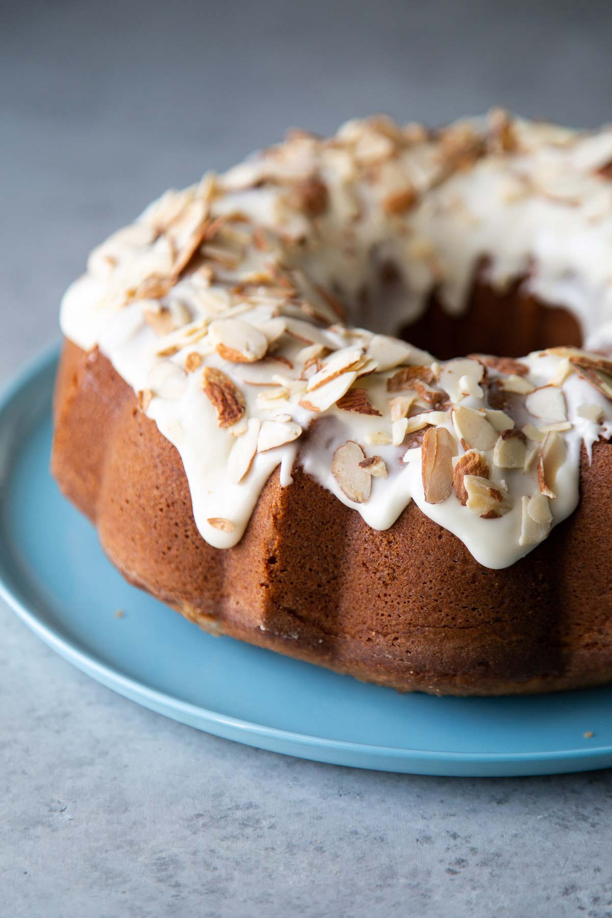 almond pound cake topped with almond glaze and toasted sliced almonds on blue plate.