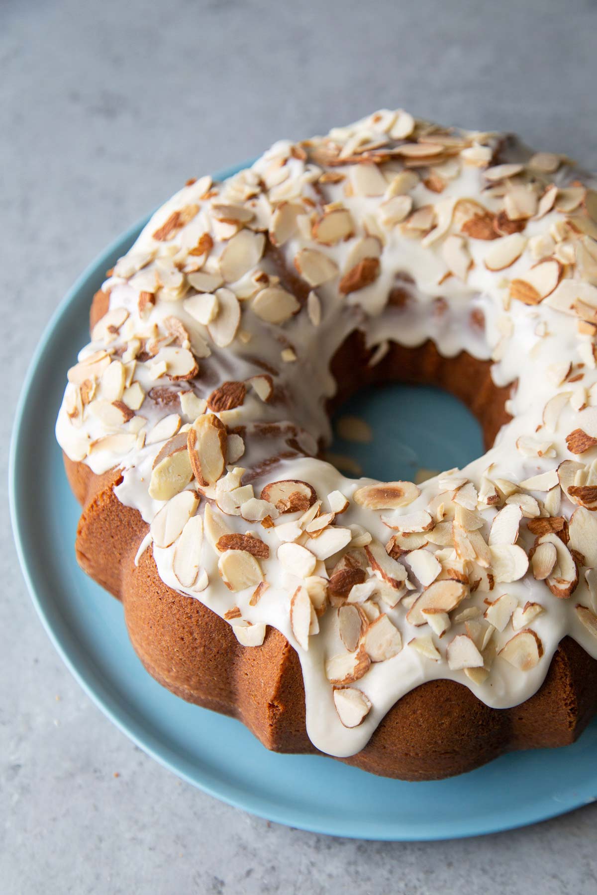 almond pound cake with almond glaze and toasted sliced almonds on blue plate.