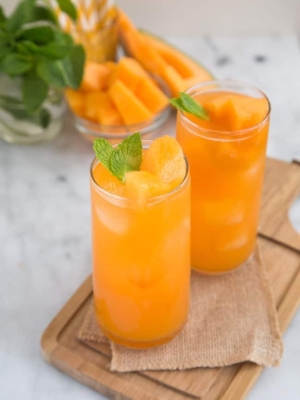 two glasses of cantaloupe agua fresca garnished with fresh mint.
