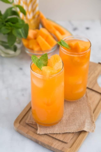 two glasses of cantaloupe agua fresca garnished with fresh mint.