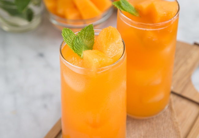 two glasses of cantaloupe agua fresca garnished with fresh mint.