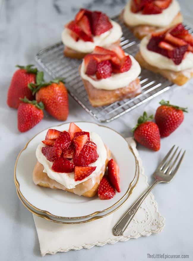 strawberry shortcake donuts with cream cheese frosting and fresh strawberries on wire rack and serving plate. 