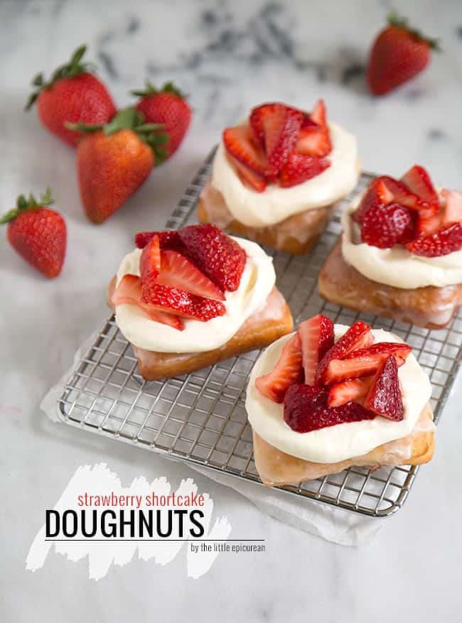 strawberry shortcake donuts with cream cheese frosting and fresh strawberries on wire rack. 