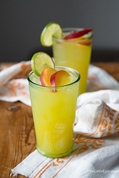 ginger peach cooler cocktail garnished with fresh peach slice and lime wheel.