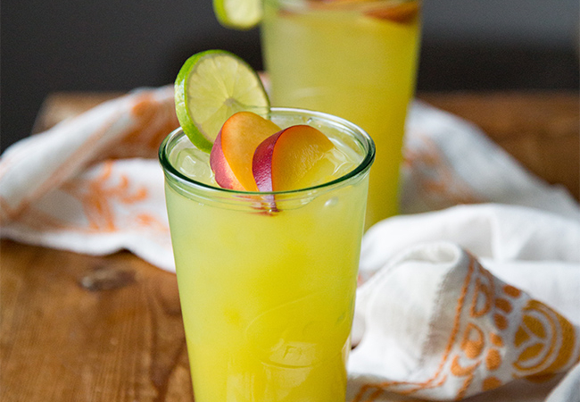 ginger peach cooler cocktail garnished with fresh peach slice and lime wheel.
