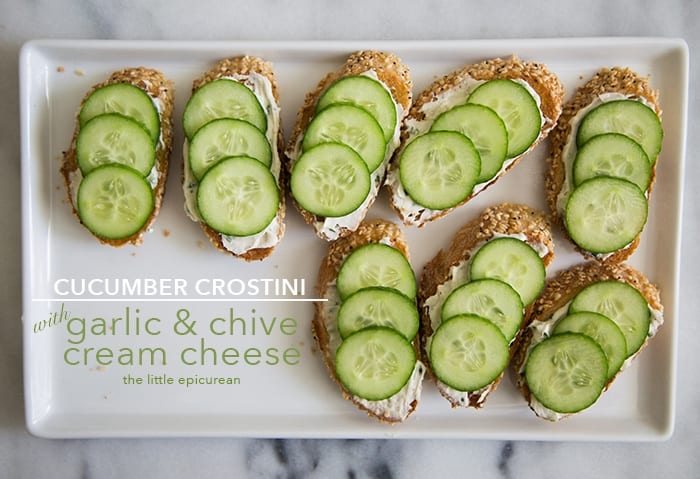 Garlic and Chive Cream Cheese spread on sliced baguette topped with sliced cucumbers on serving plate. 