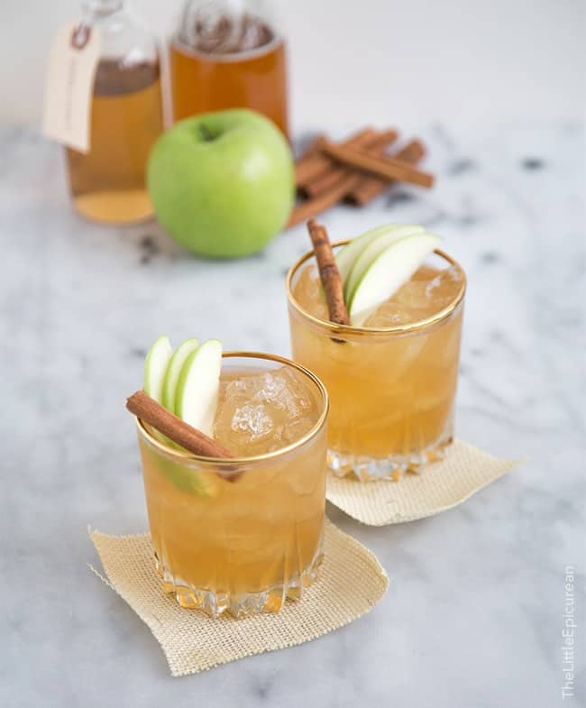 Two servings of apple pie moonshine cocktail garnished with apple slices and cinnamon stick. 