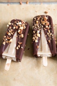 Banana Coconut Ice Pops with dipped in chocolate and almonds in a row on parchment paper.