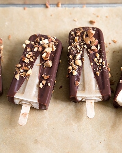 Banana Coconut Ice Pops with dipped in chocolate and almonds in a row on parchment paper.
