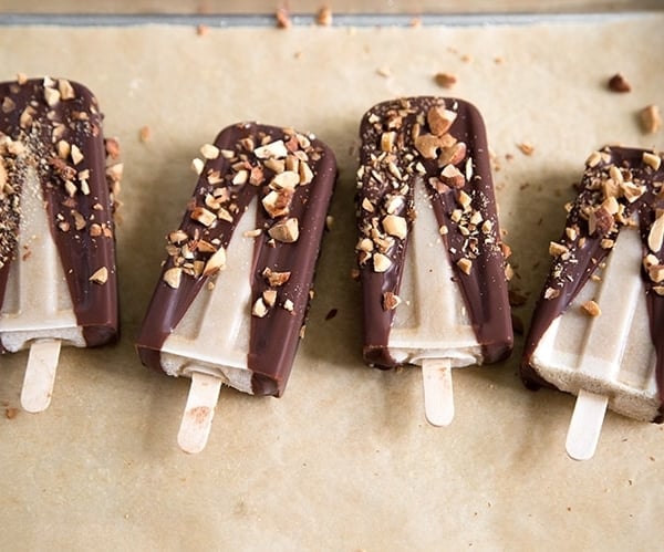 Banana Coconut Ice Pops with dipped in chocolate and almonds in a row on parchment paper.
