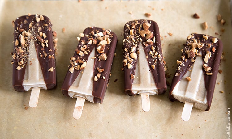 Banana Coconut Ice Pops with dipped in chocolate and almonds in a row on parchment paper.